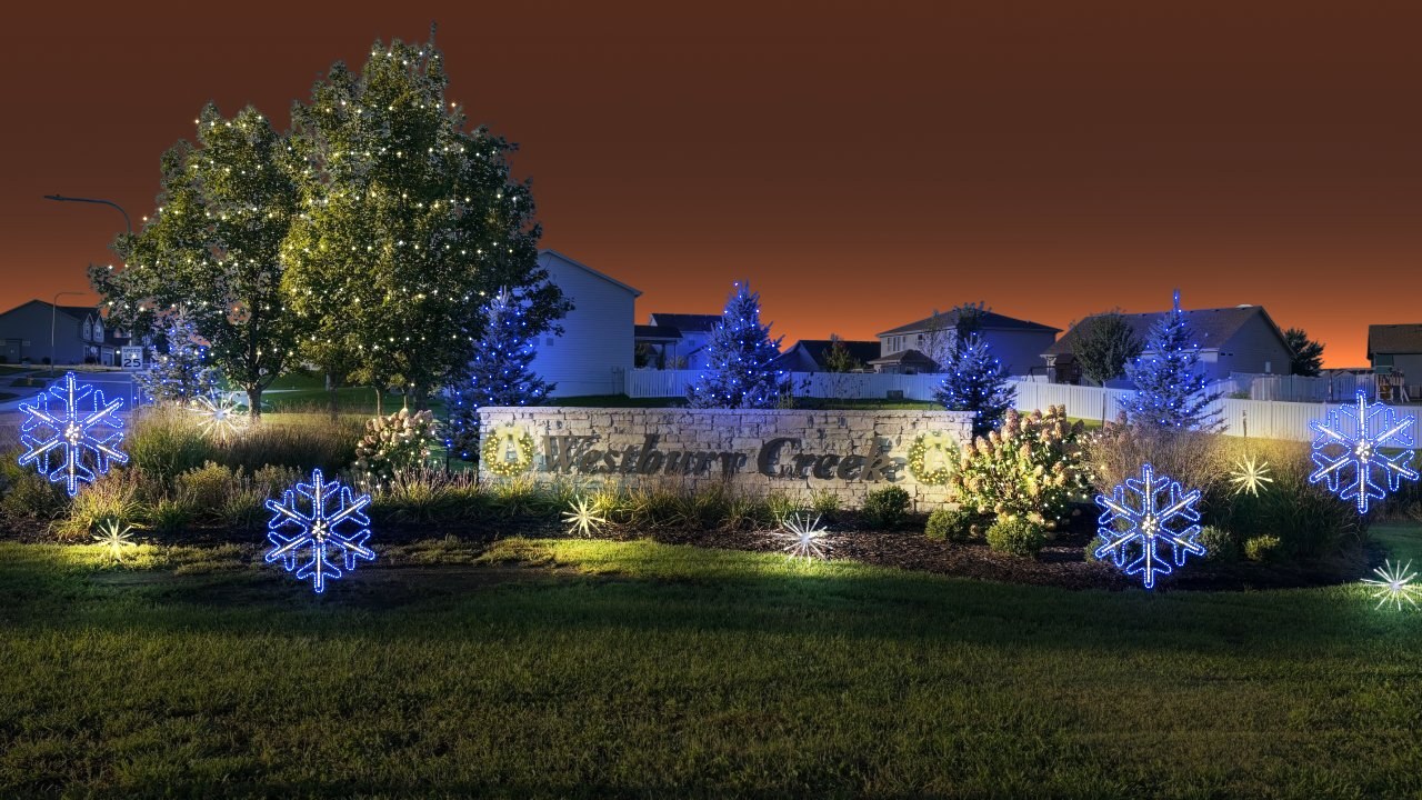 Glow Getter design rendering: monument sign framed in warm wreaths, entry trees wrapped in warm and cool white, and lit snowflakes and starbursts through the beds.