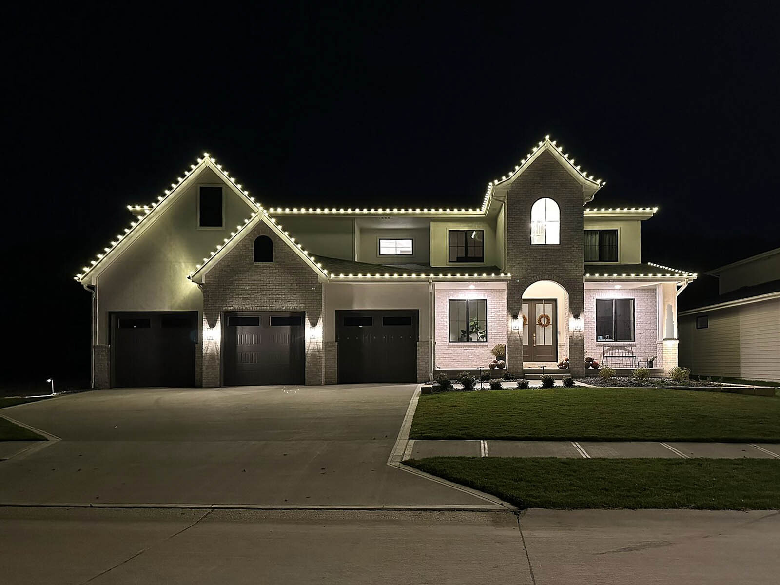Farmhouse-style home with roofline and covered porch traced in warm white christmas lights