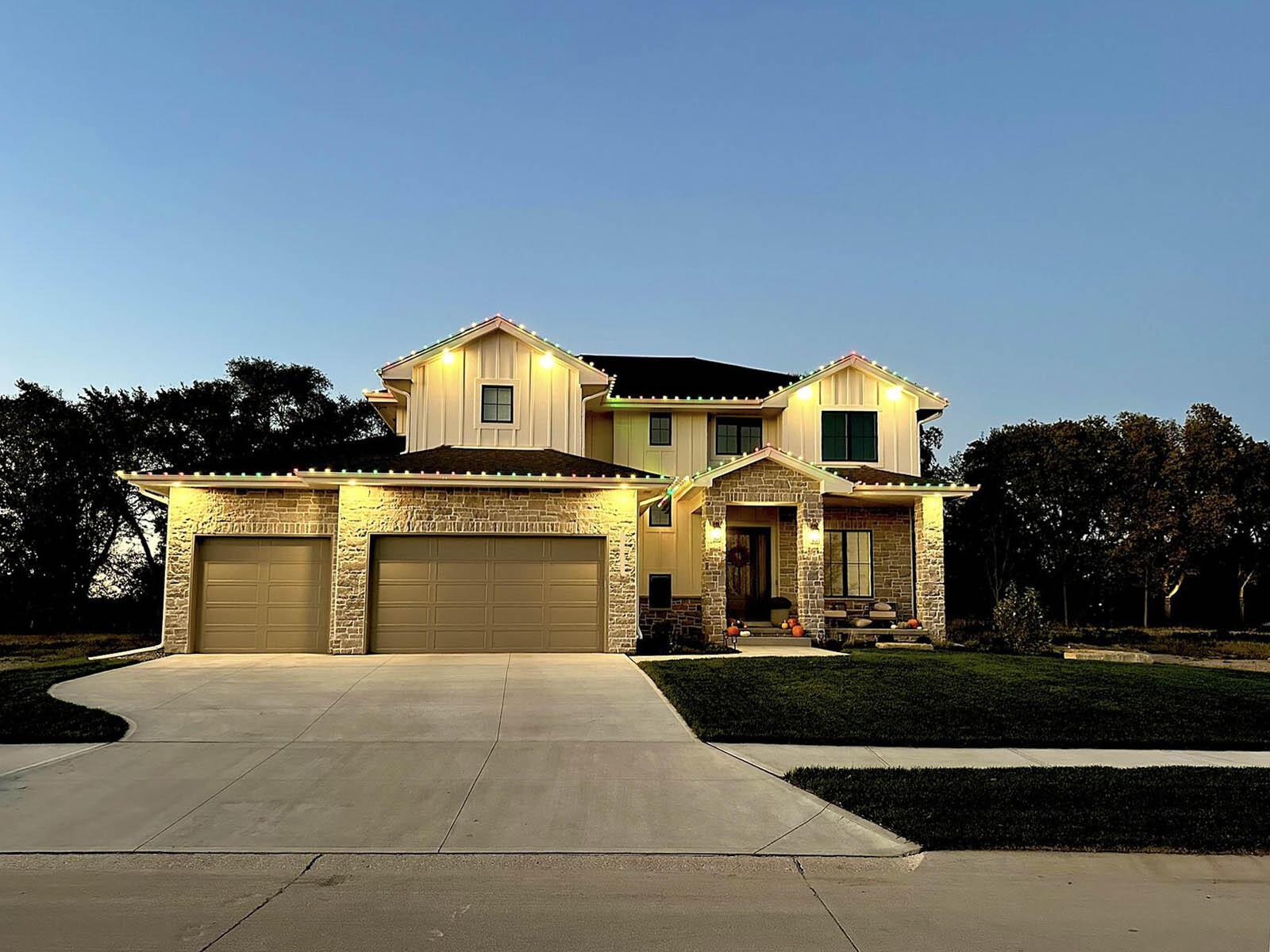 Two-story home glowing with warm white christmas lights against a twilight sky