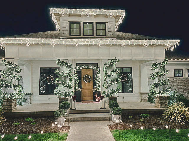 Craftsman home with snowflake roofline lighting over garland-wrapped columns